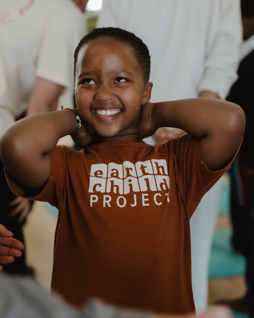 A child in an Earthchild Project t-shirt smiling with hands behind their head.