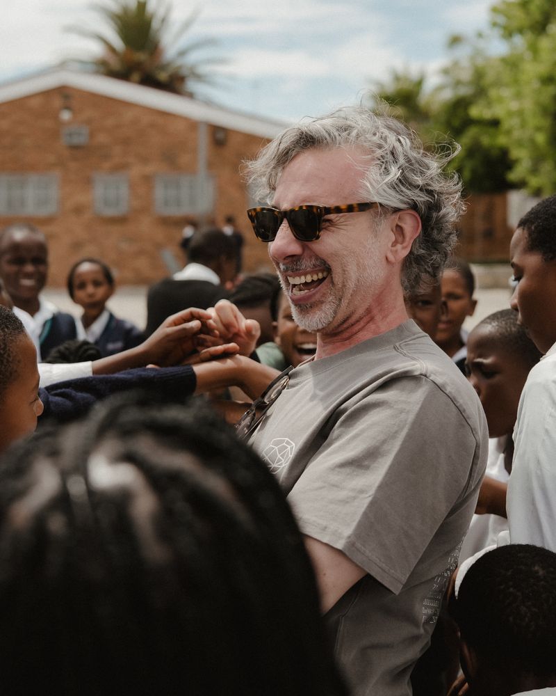 A visitor laughing in the middle of a crowd of schoolchildren.