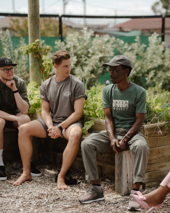 Visitors and an Earthchild facilitator sitting together on the edge of a raised garden bed.