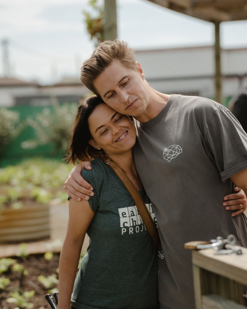 Two people embracing in the school garden, one wearing an Earthchild Project shirt.