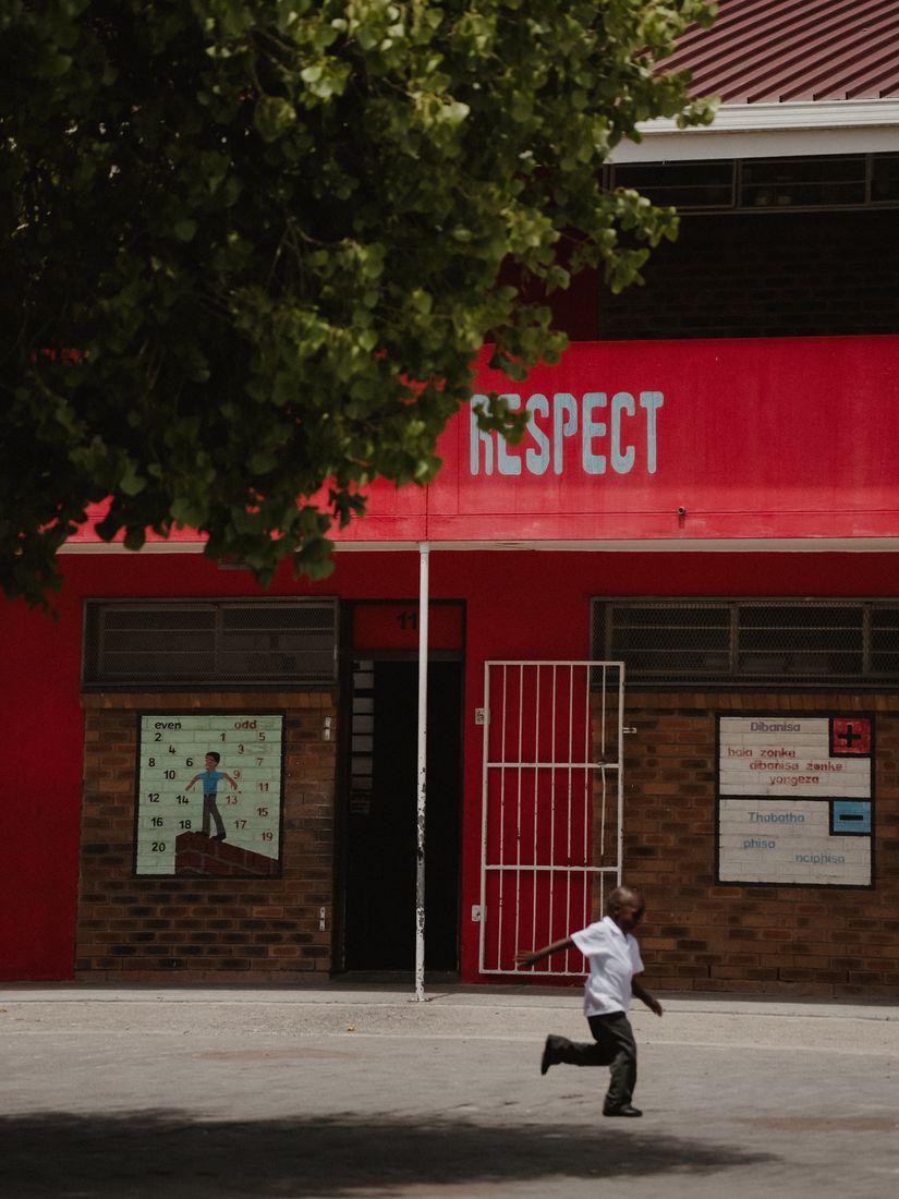 A child running across the school yard beneath the word RESPECT painted on a red wall.