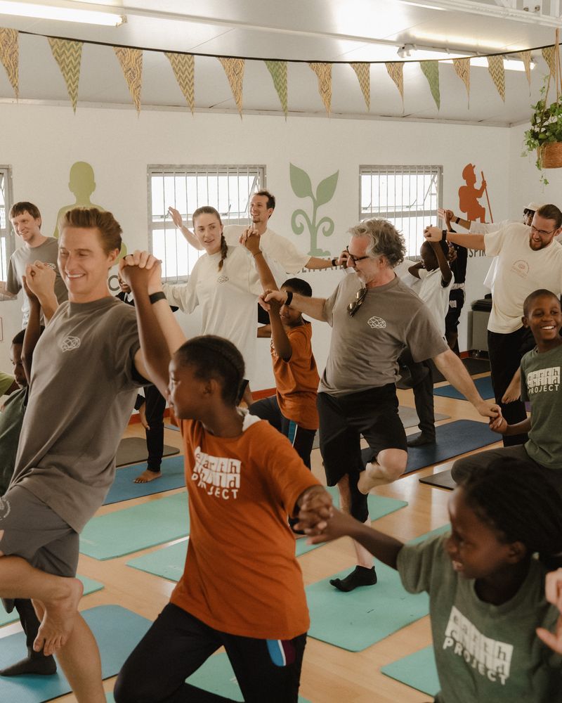 Children and visitors balancing on one leg together in a yoga class.